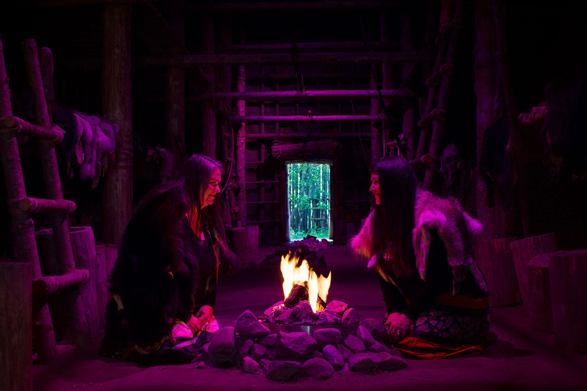 Deux femmes face à face devant un feu de camp dans une maison longue traditionnelle
